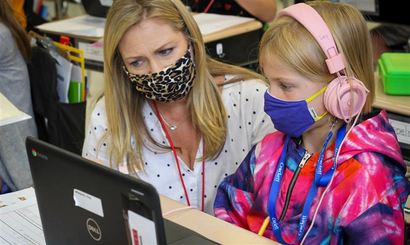Teacher helps student on laptop